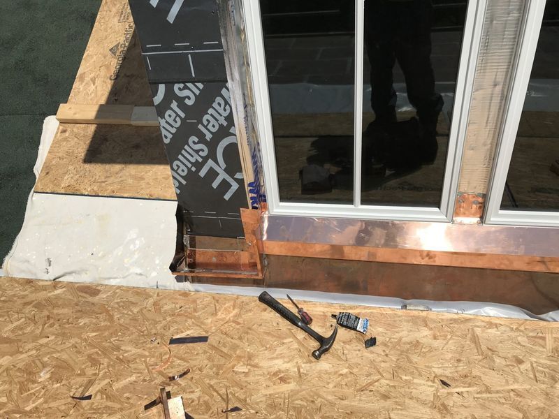 Copper flashing installed around a window frame on an OSB roof deck. Hammer and tools nearby.