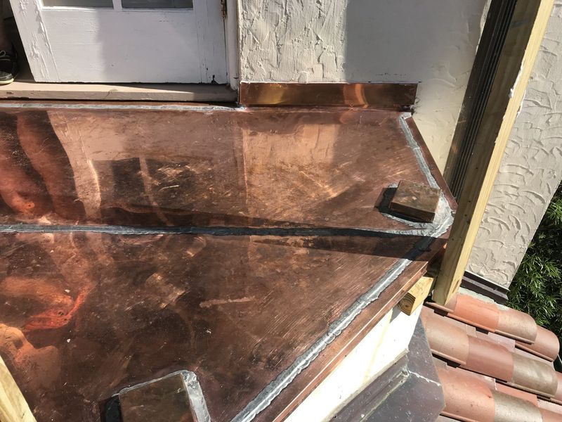 Copper flashing on a roof, near a door. The metal has a dark, aged appearance.