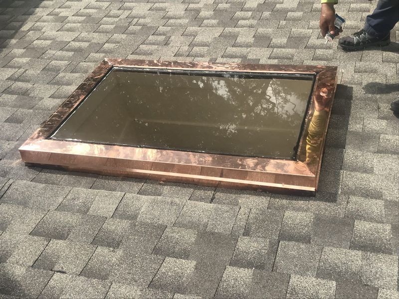 Copper-framed skylight on a gray shingle roof, reflecting the sky.