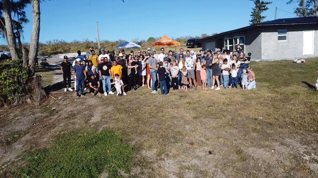 Large group of people posing together outdoors on a sunny day in front of a building.