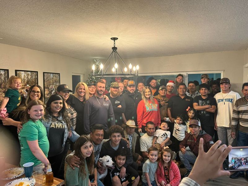 Large group of diverse people smiling for a photo in a warmly lit room, possibly a family gathering.