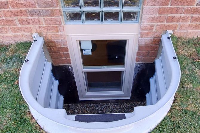 White window well with window in light brick wall, brown mulch.