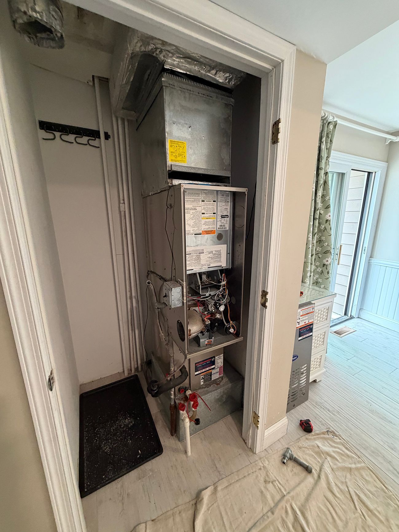 An HVAC furnace unit with its metal cover removed, installed inside a small utility closet in a bright home interior.