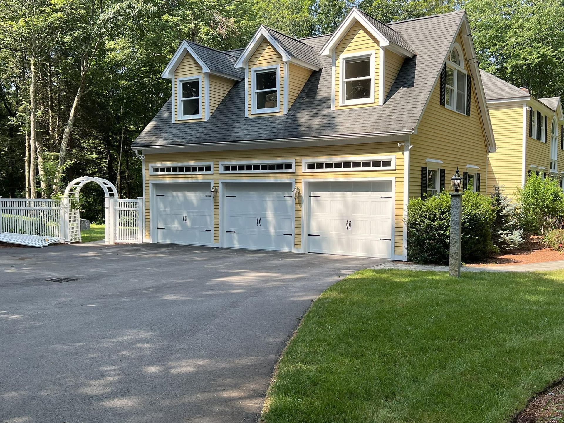 Yellow house with three garage doors, dormers, and a driveway.
