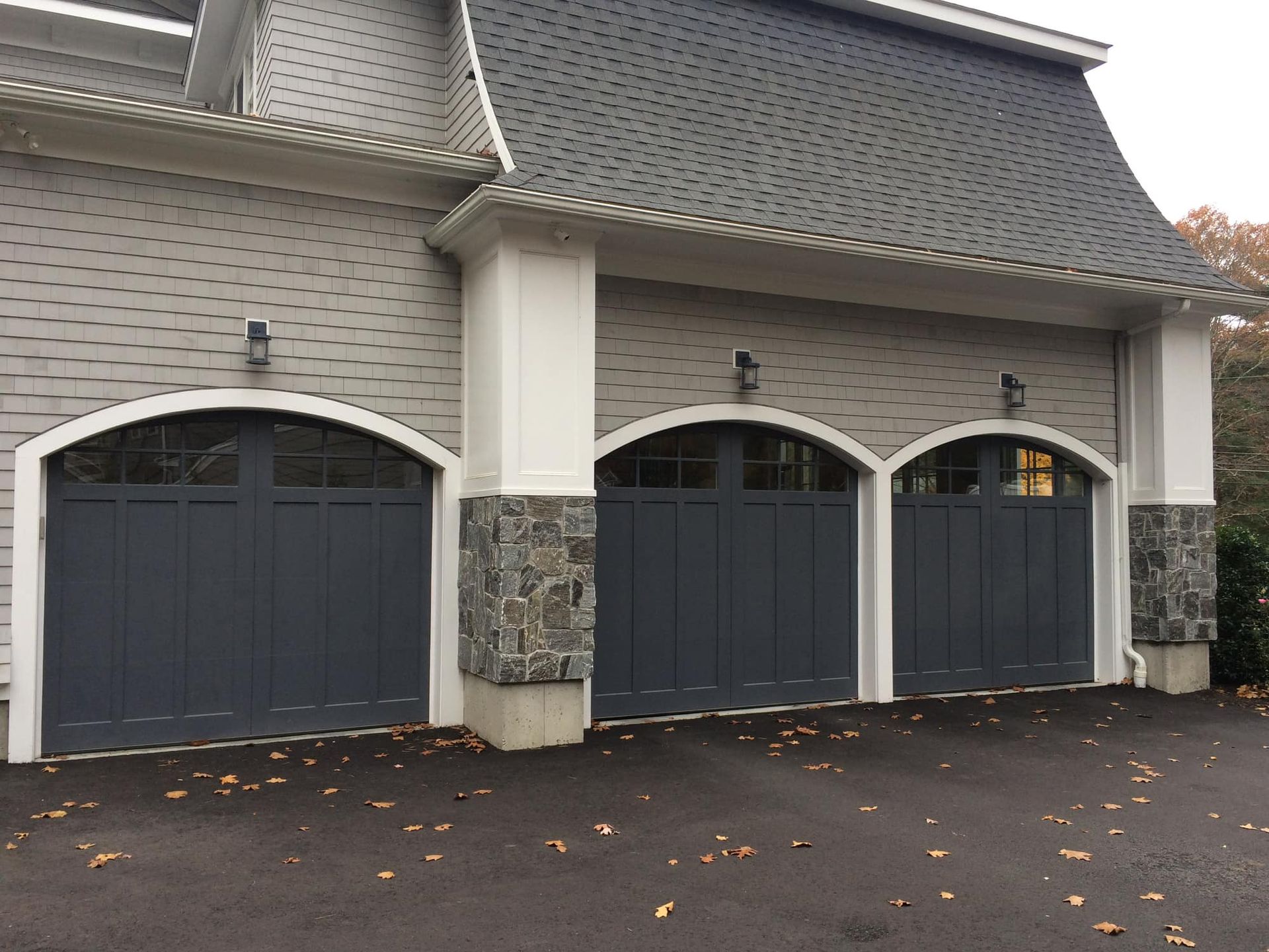 Gray garage doors on a light gray building with stone columns, set against a gray roof.