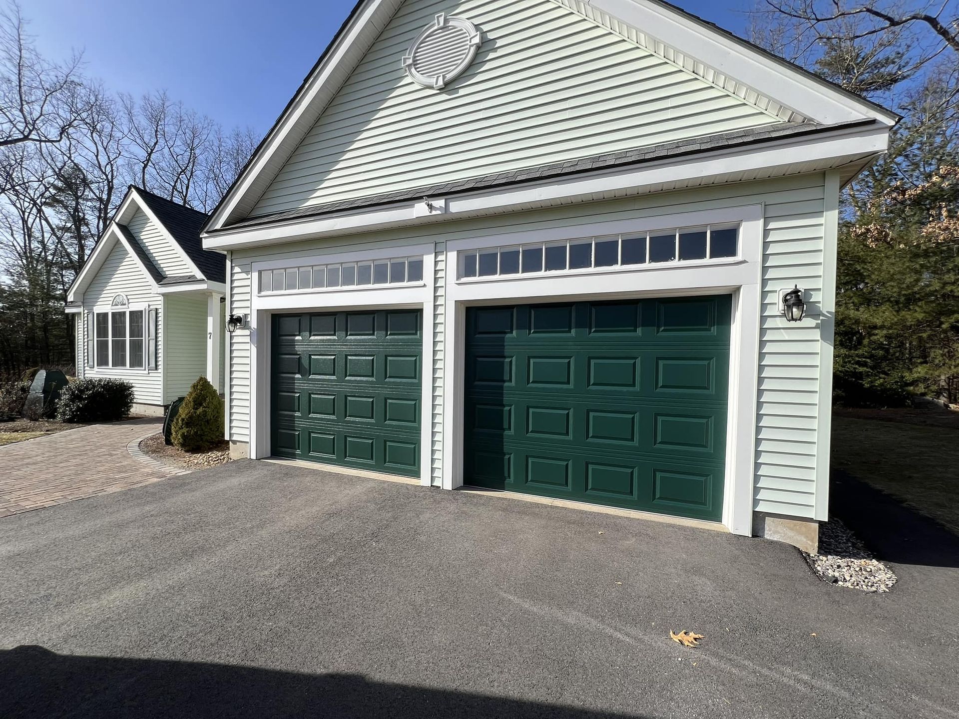 Green garage doors on a light green building with a driveway.