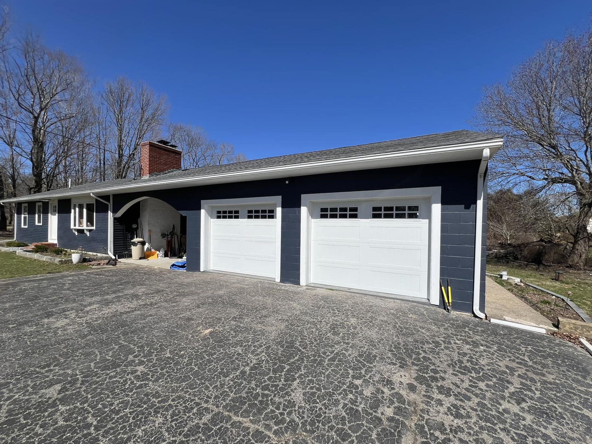 Blue house with white garage doors, dark driveway, clear sky.