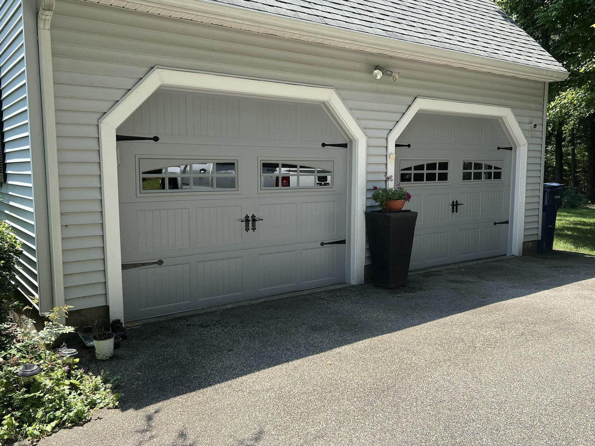 Two gray garage doors with decorative black hardware on a gray house.