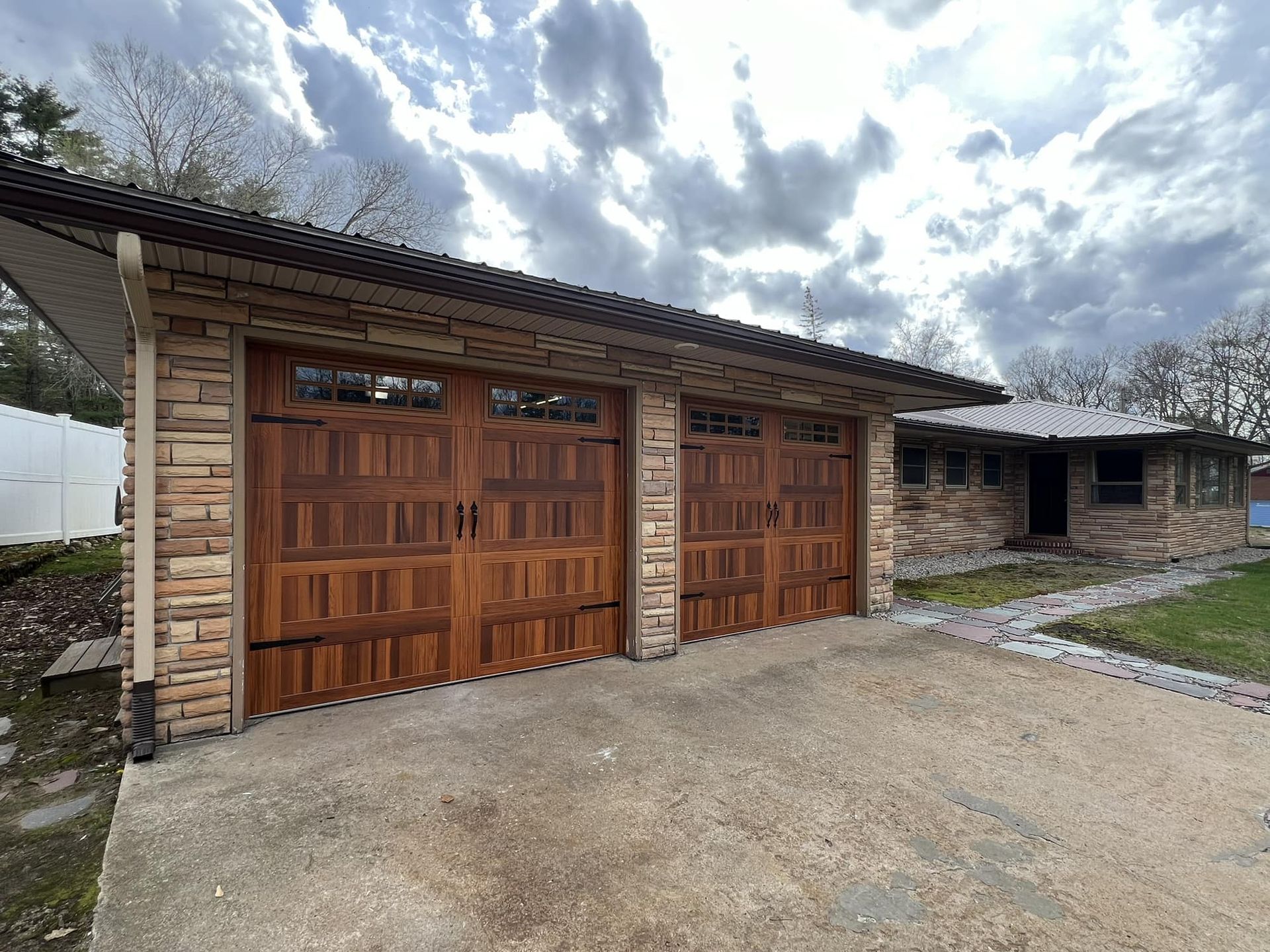 Brown garage doors with stone facade. Concrete driveway. Cloudy sky.