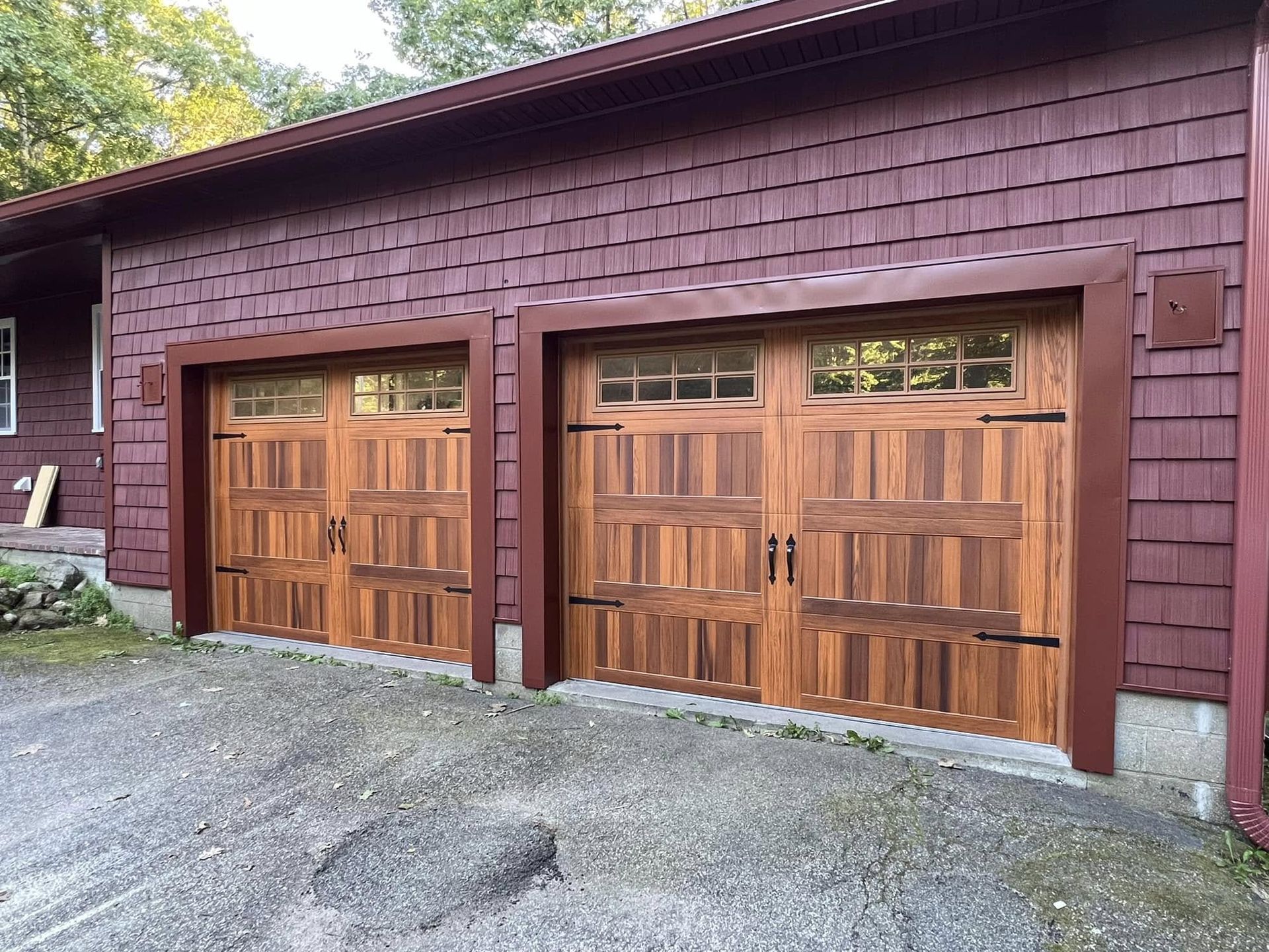 Two wooden garage doors with glass panels, brown trim, on a building with red siding.