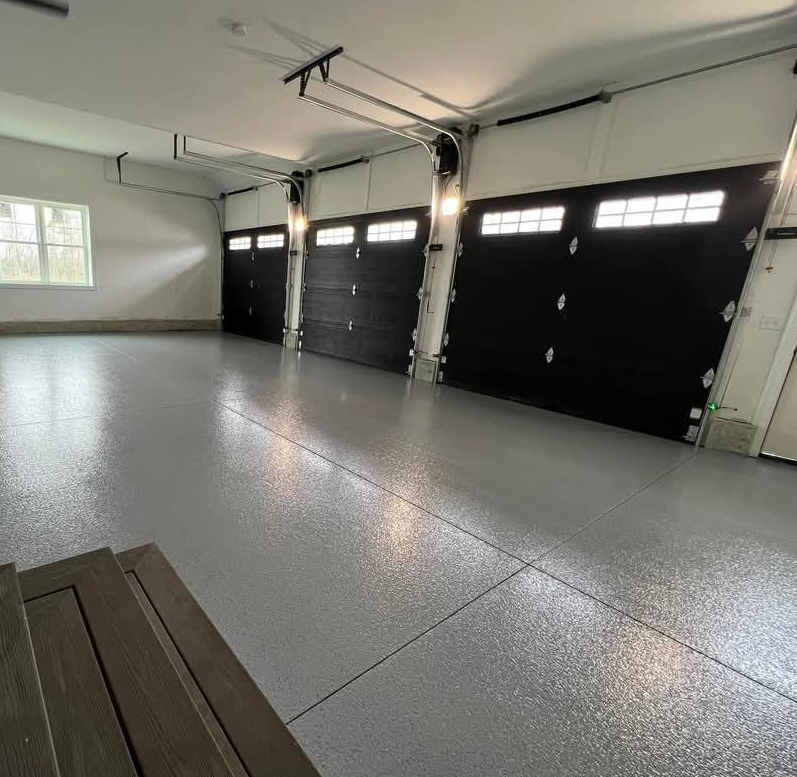 A gray-floored garage with three black doors, windows, and a wood bench.