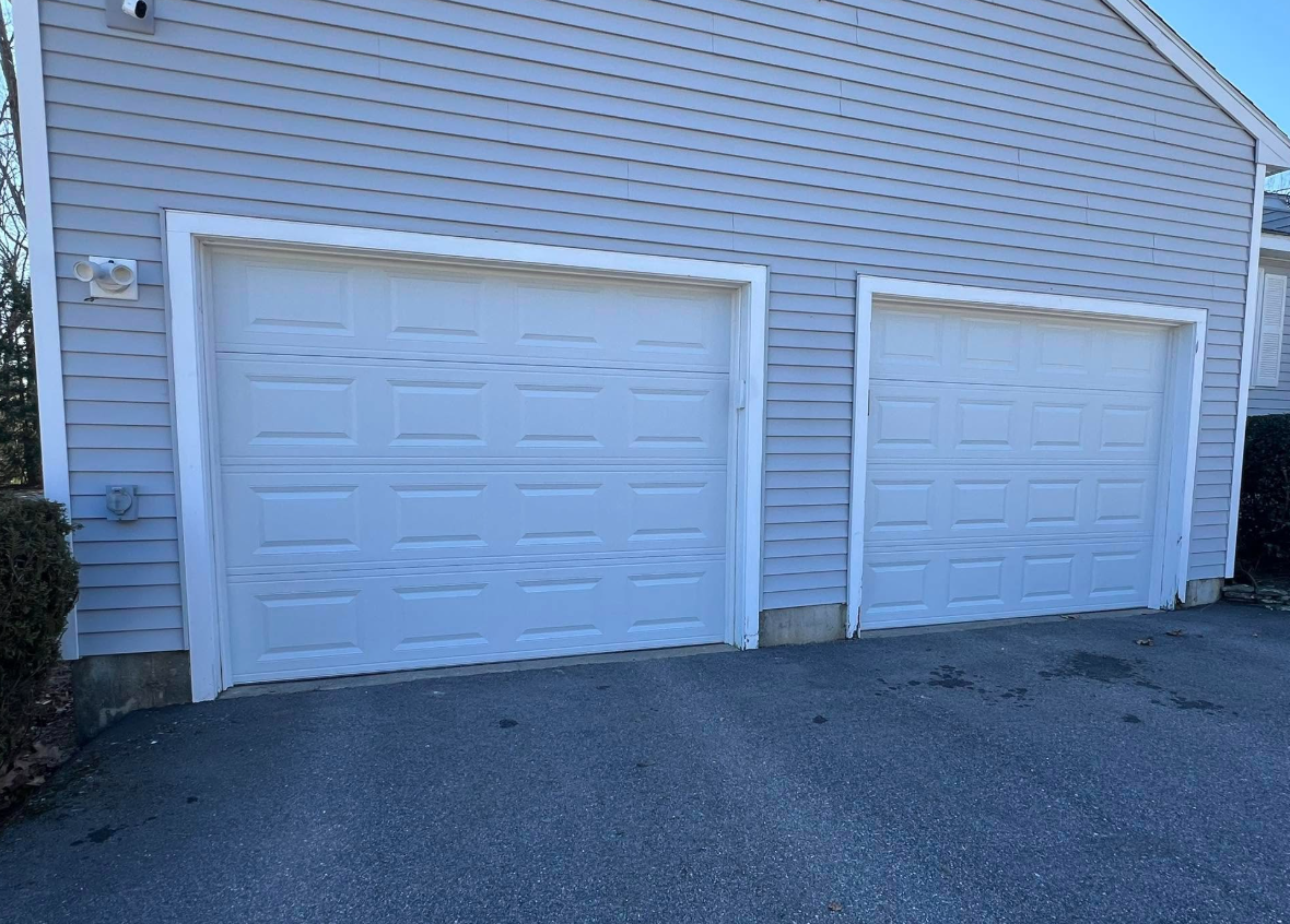 Two white garage doors on a light blue building. Asphalt driveway in front.