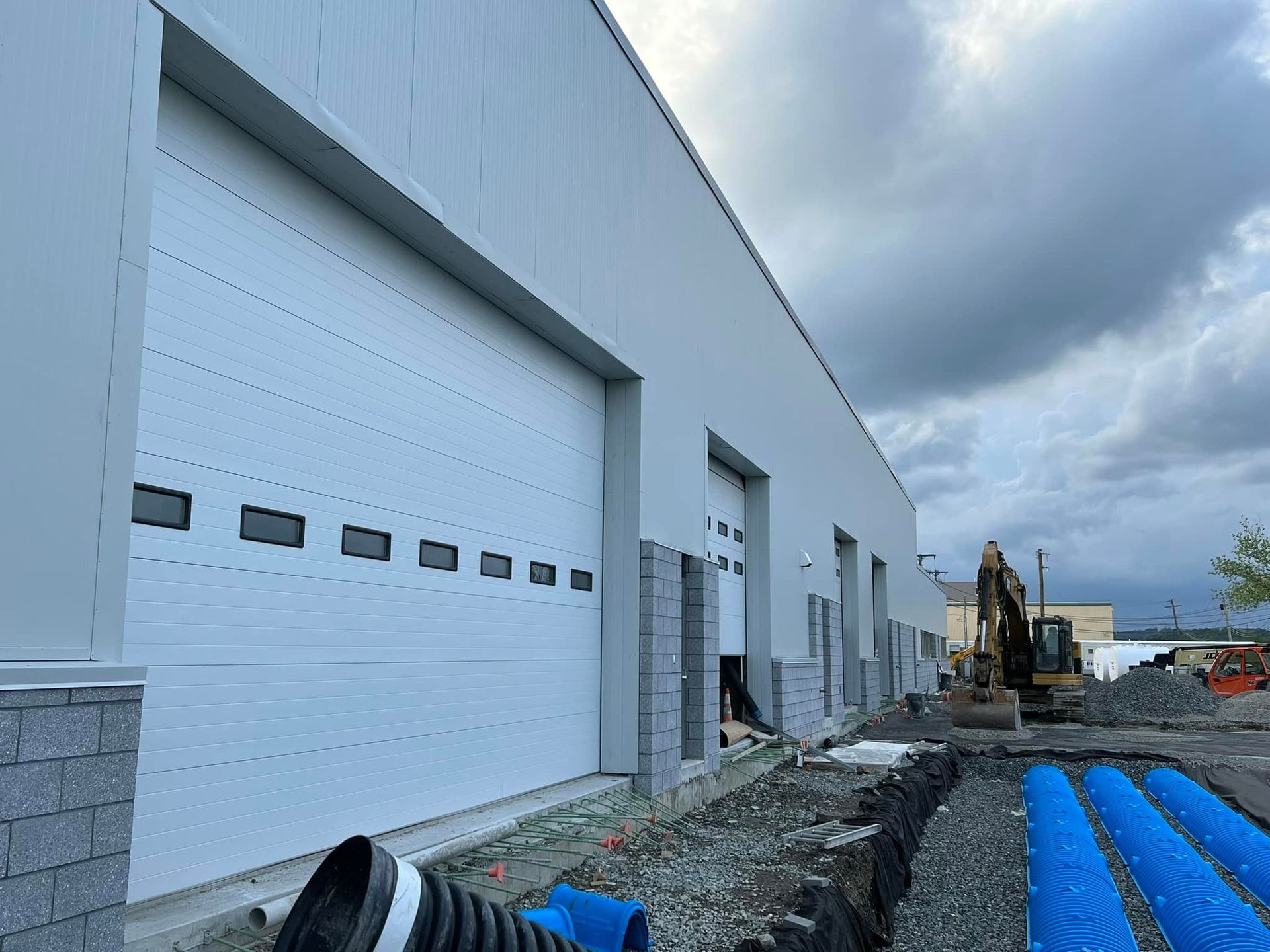Exterior of a commercial building under construction with large garage doors and an excavator.