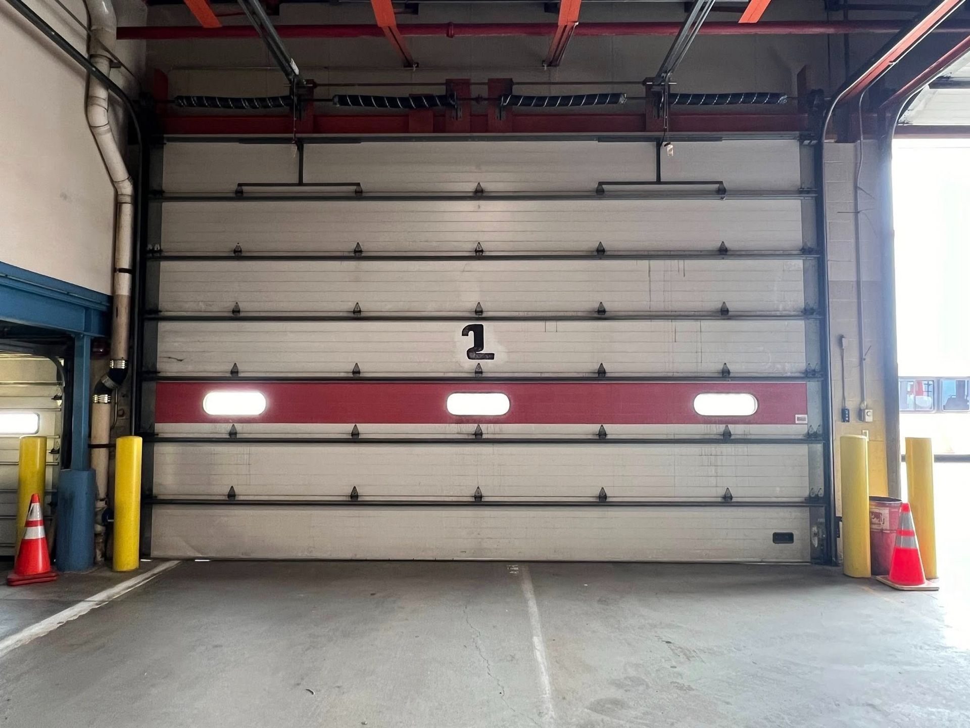 Closed loading dock door, red stripe, number 1. Yellow bollards, concrete floor.