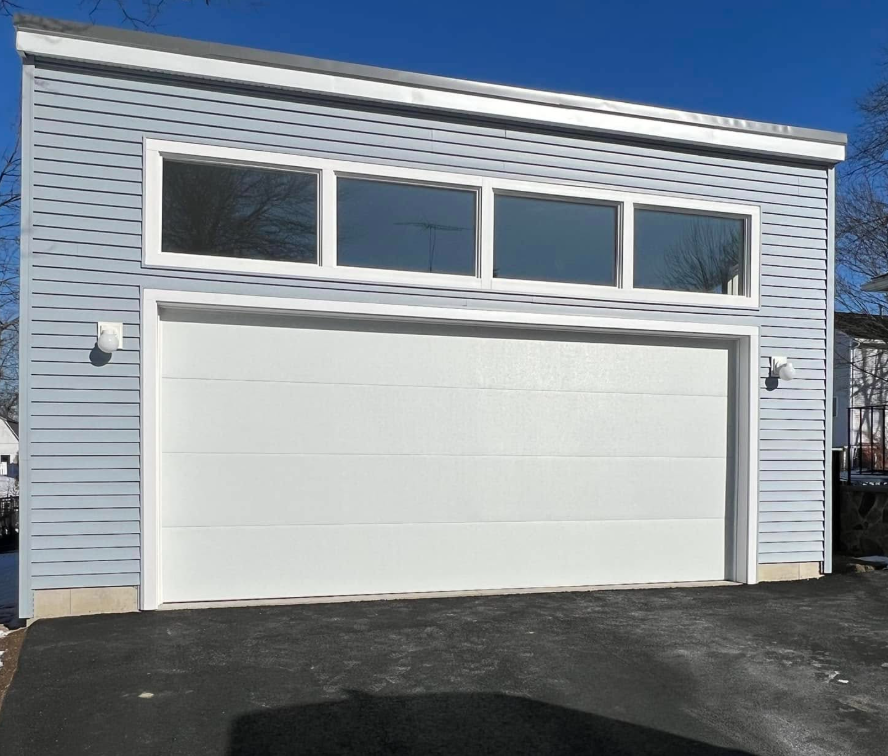 Blue-gray garage with white door, windows, and trim. Bright day, asphalt driveway.