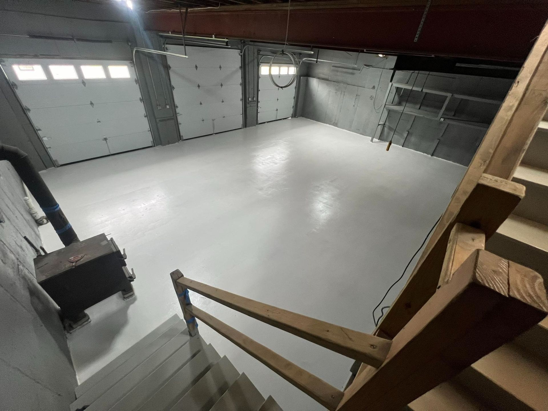 Basement with light gray floor, stairs, and storage shelves. A wood-burning stove sits to the left.