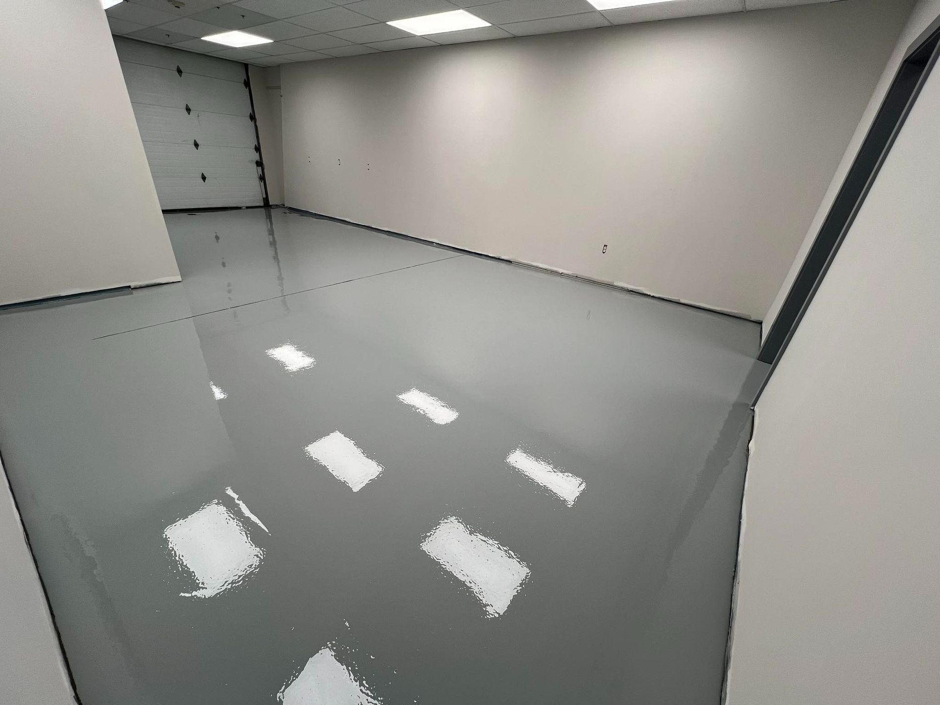 Empty room with gray epoxy floor and white walls. Light reflecting on the shiny surface.