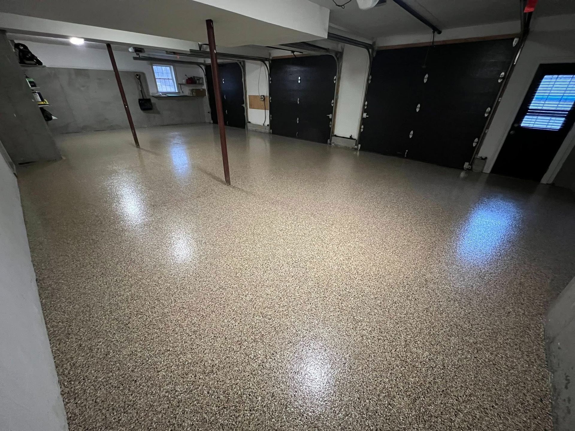 Garage with speckled flooring, black doors, support beams, and a window.