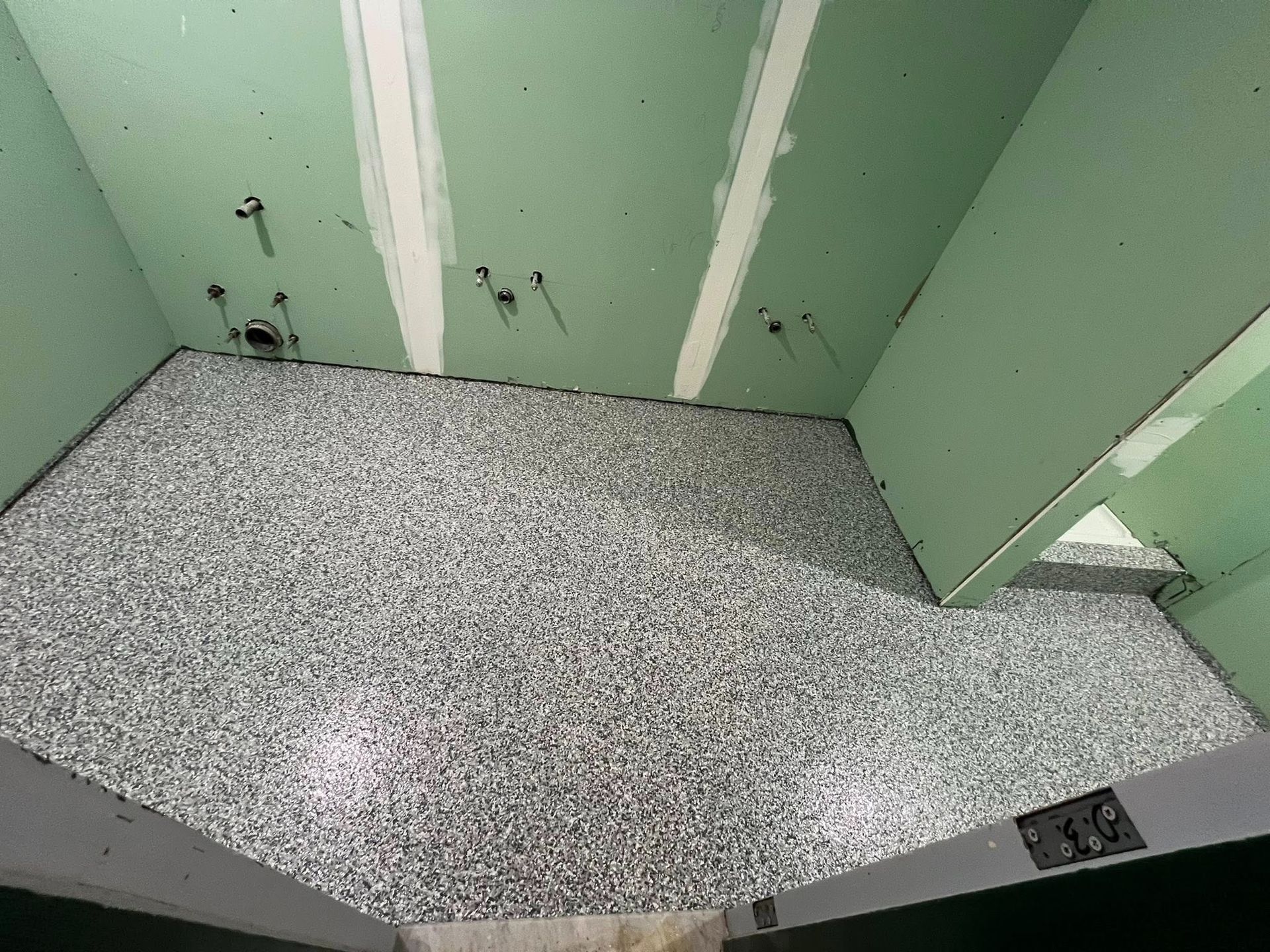 Room with speckled gray flooring, light green walls, and exposed plumbing fixtures.