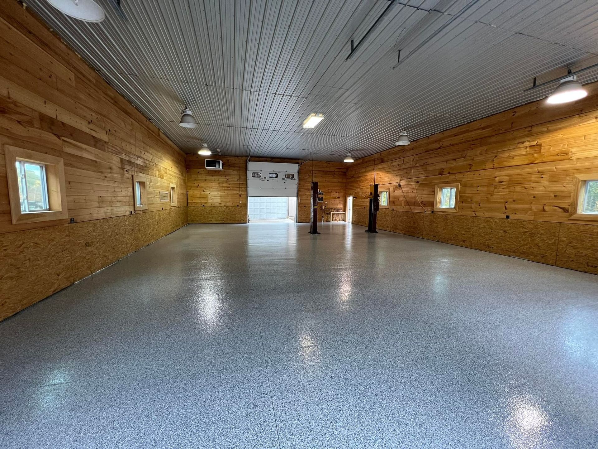 Spacious, empty garage with a shiny, speckled floor, wooden walls, and corrugated metal ceiling.