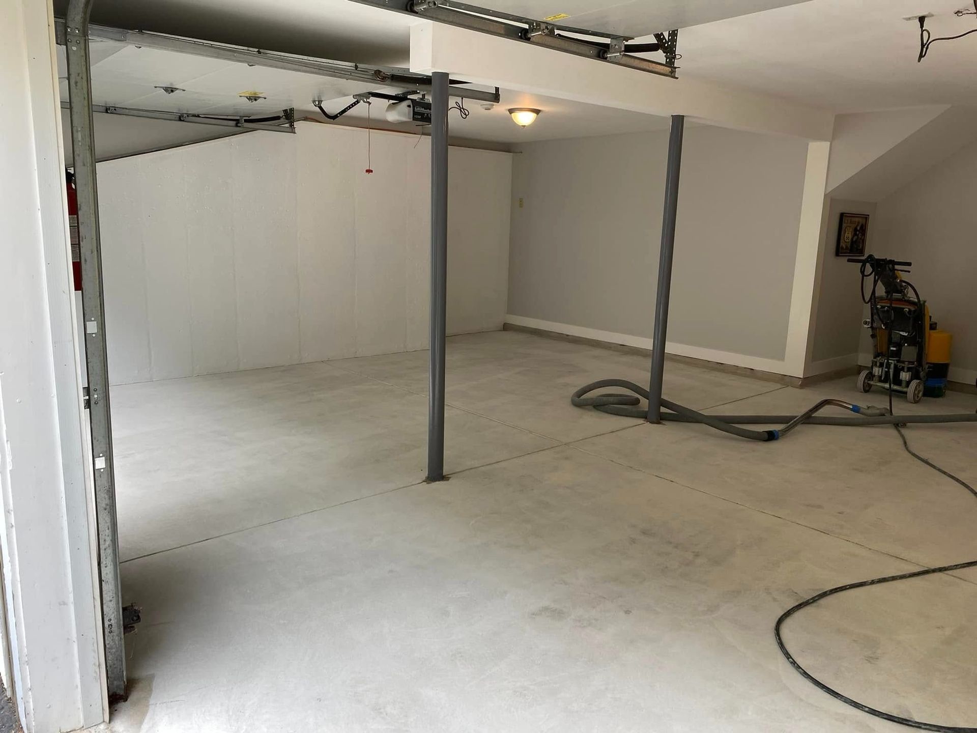 Interior view of a freshly painted garage with concrete floor, support columns, and grinding machine.