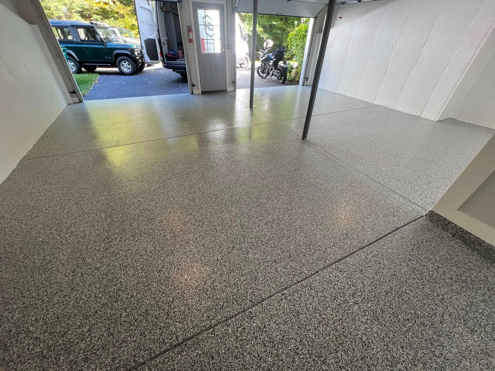 Epoxy-coated garage floor with gray and white chips. Open garage door with vehicle in the background.