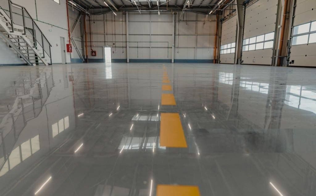Spacious, empty gray warehouse interior with shiny floor, yellow line, windows, and stairs.