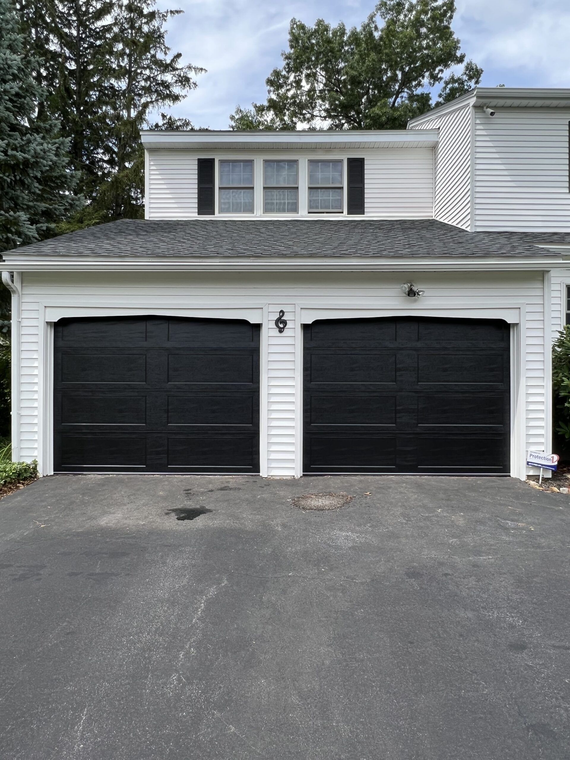 Two black garage doors on a white house, with a dark driveway.