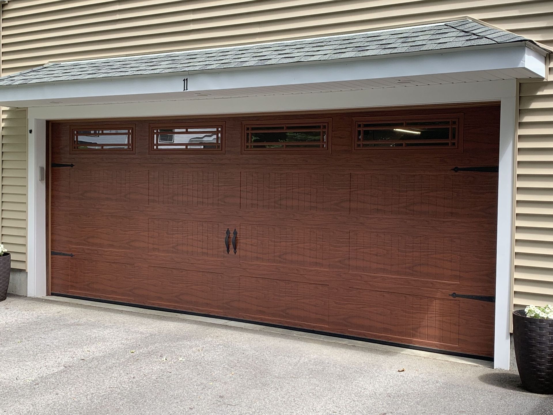 Brown garage door with windows and black hardware, in front of a light brown house.