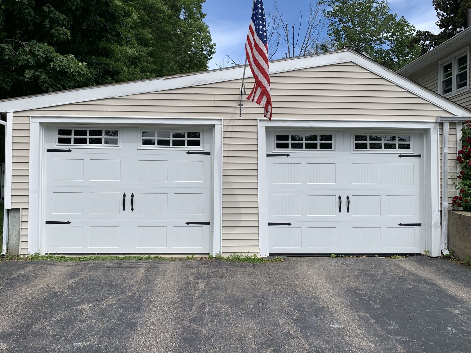 Two-car garage with white doors, black hardware, American flag, and asphalt driveway.
