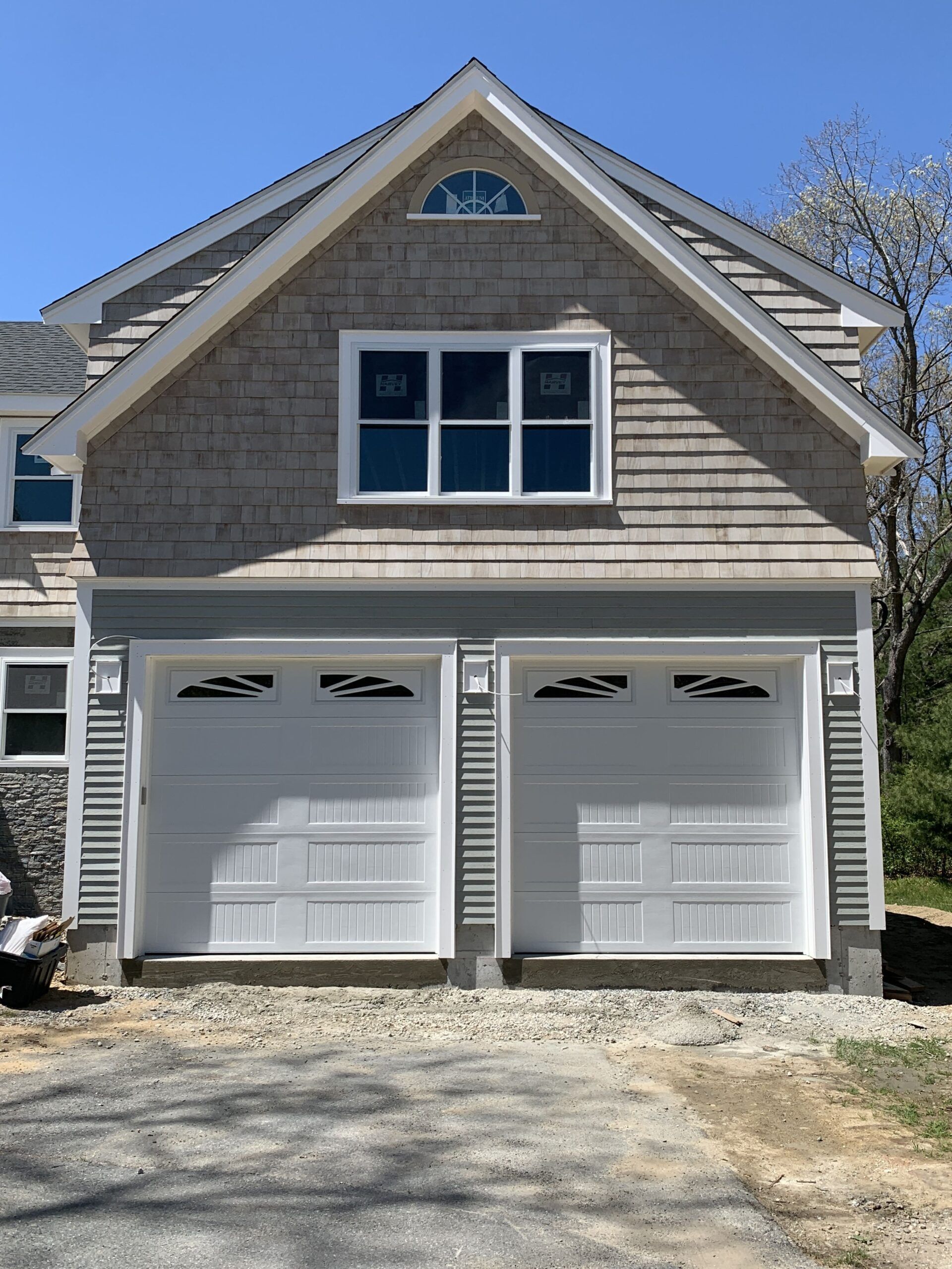 Two-car garage with white doors, surrounded by gray siding. Above are windows, and a small arched window at the peak.