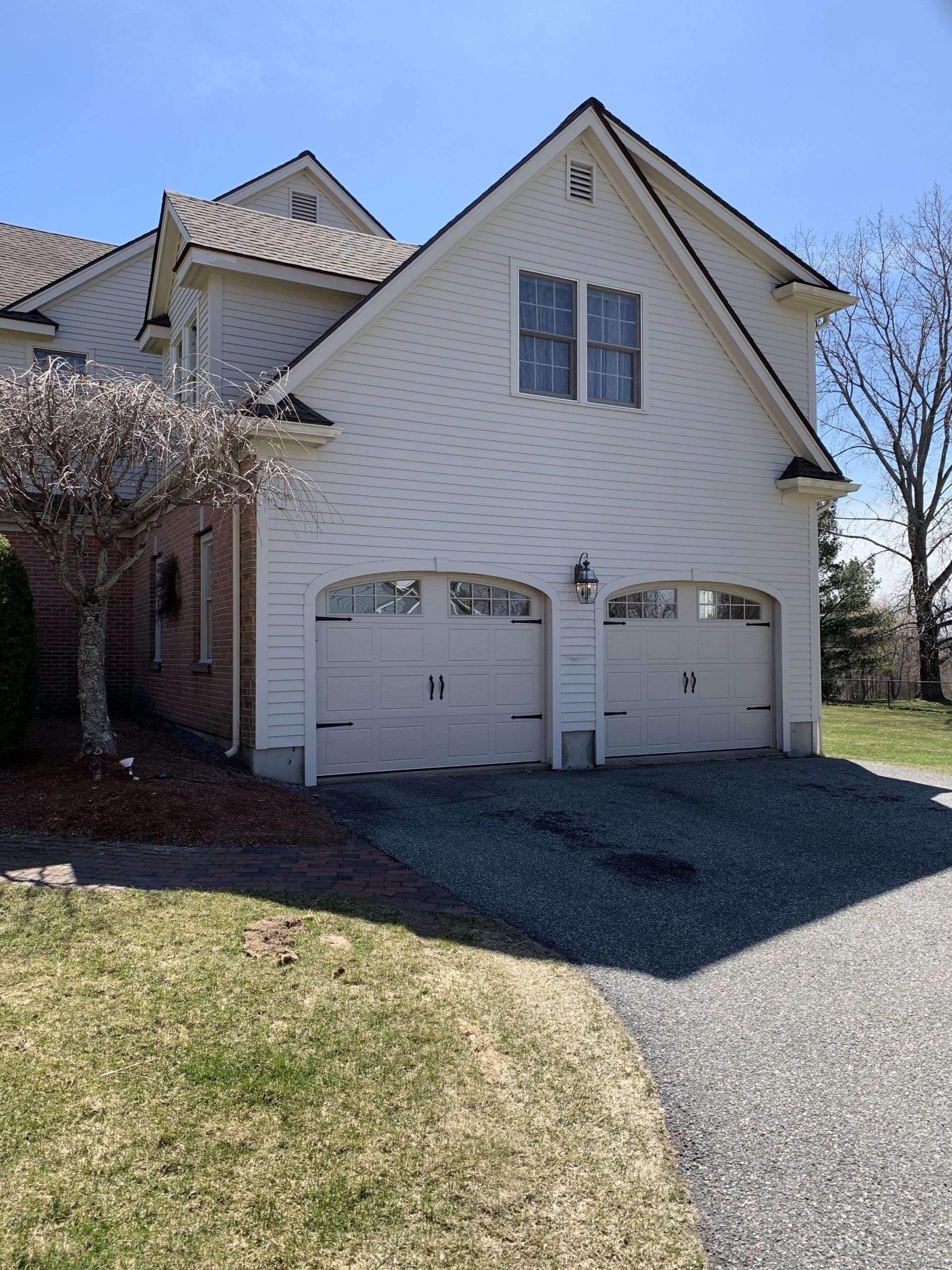 White house with two garage doors; a gravel driveway, grass, and a tree are in front.