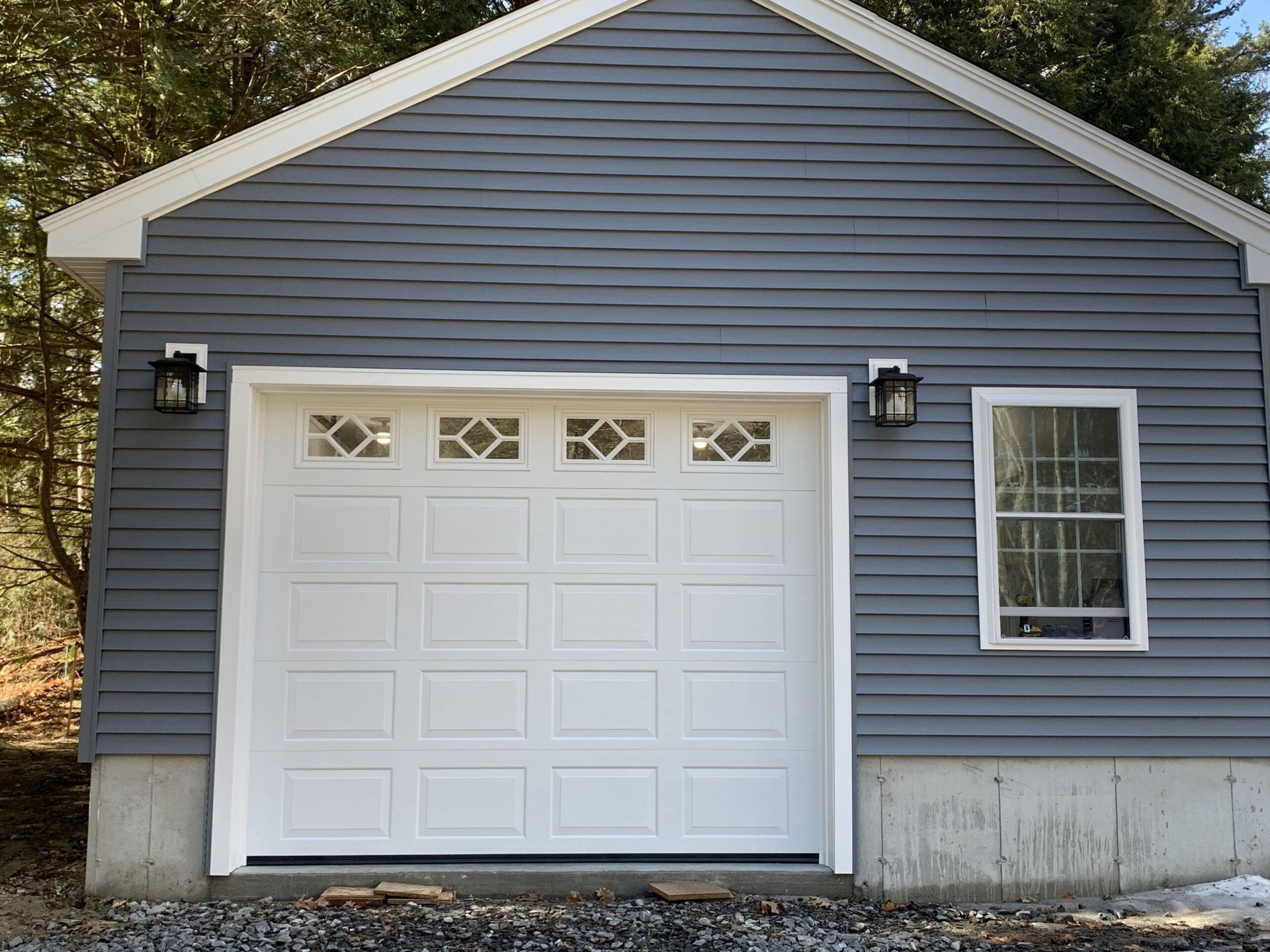 Gray garage with white door, window, and lights. Exterior view, daylight.