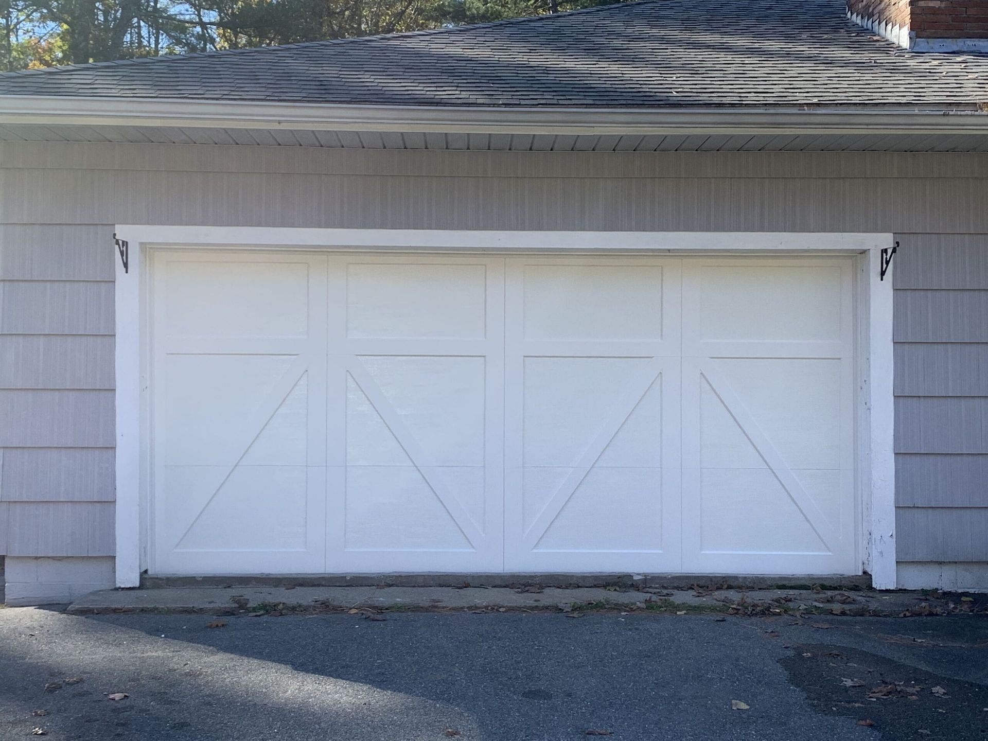 White garage door with farmhouse style design, set in a gray-sided building.