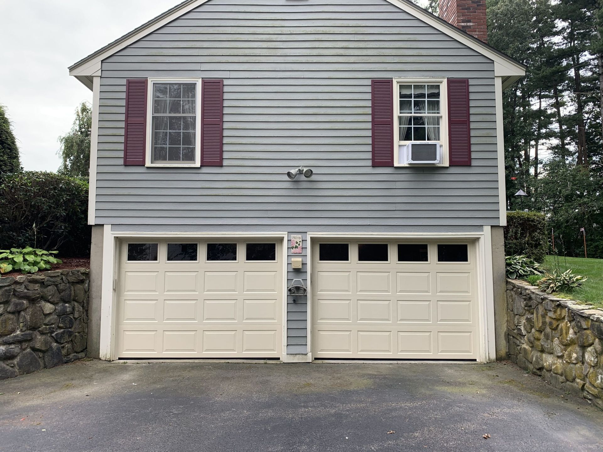 Two-car garage with cream-colored doors, gray siding, burgundy shutters, and an asphalt driveway.