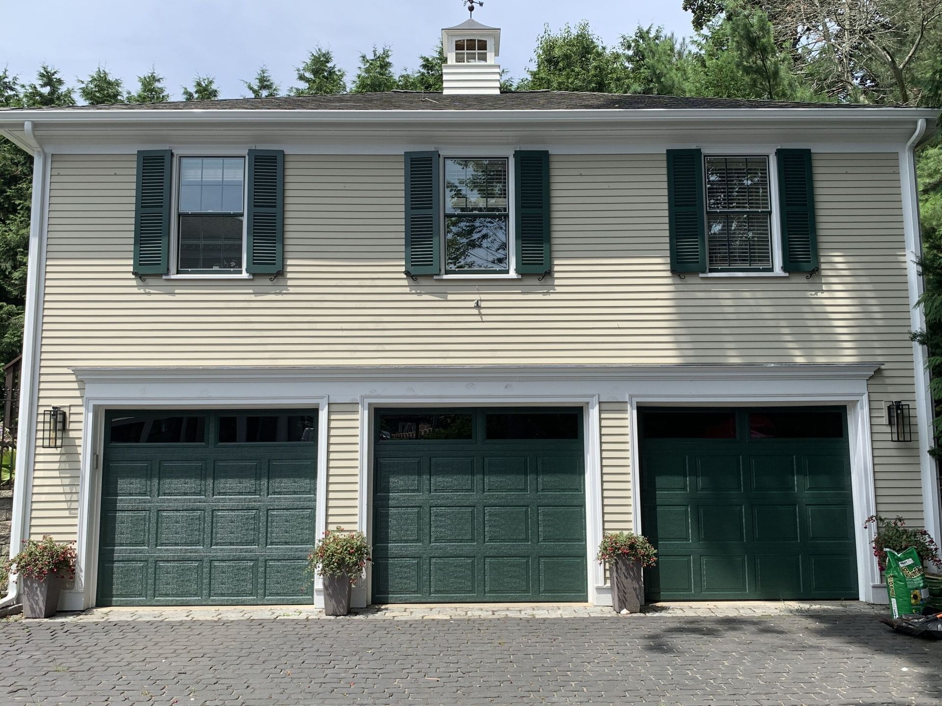 Three-bay garage with green doors and shutters; beige siding, cupola on the roof.