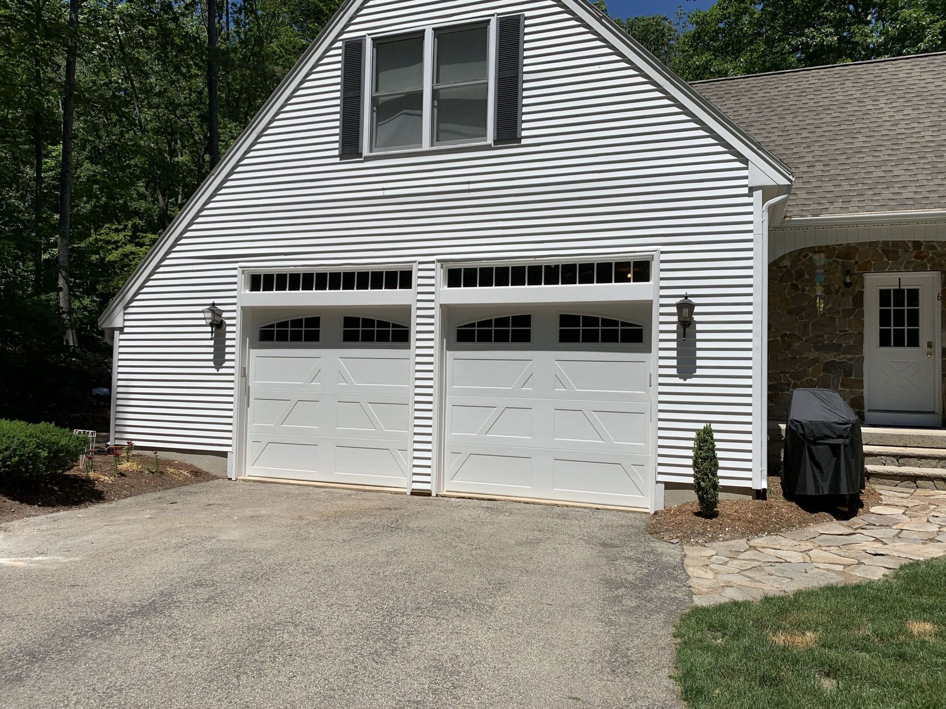 White two-car garage with two doors, a window, and black shutters. A paved driveway and stone path in front.