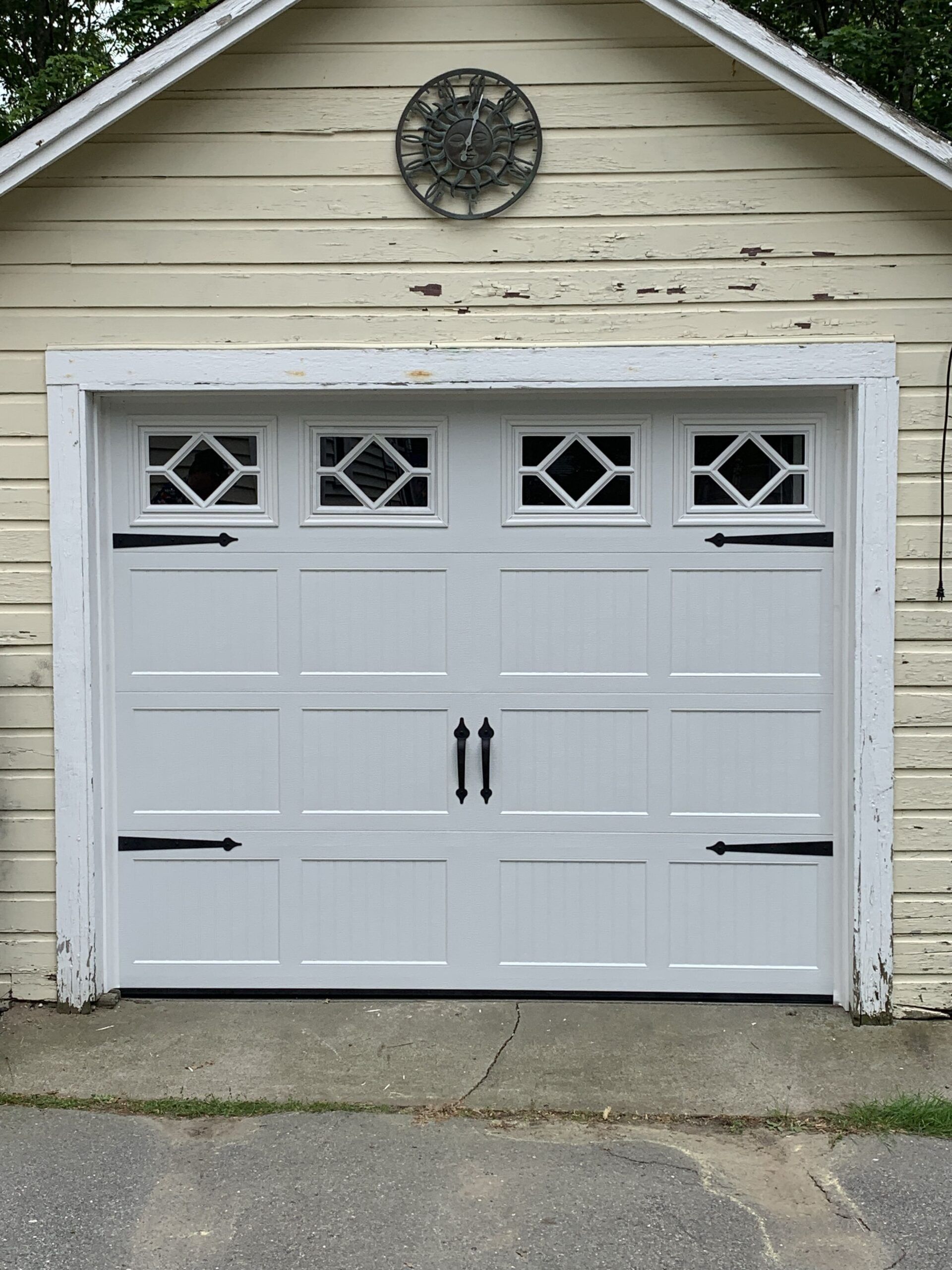 White garage door with diamond-shaped windows, black hardware, set in a weathered, cream-colored garage.