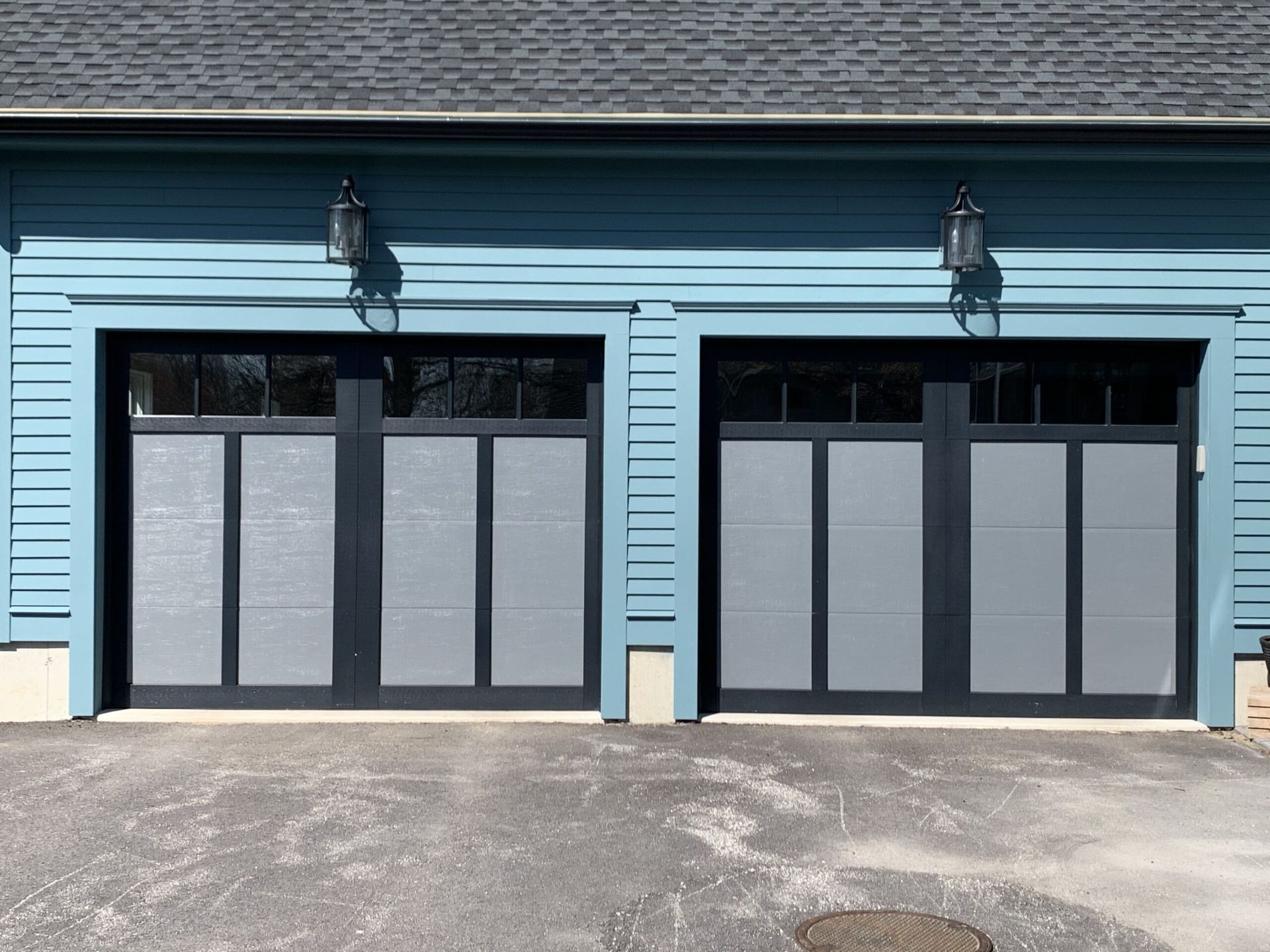 Two blue garage doors with frosted windows, black trim, and matching lights.