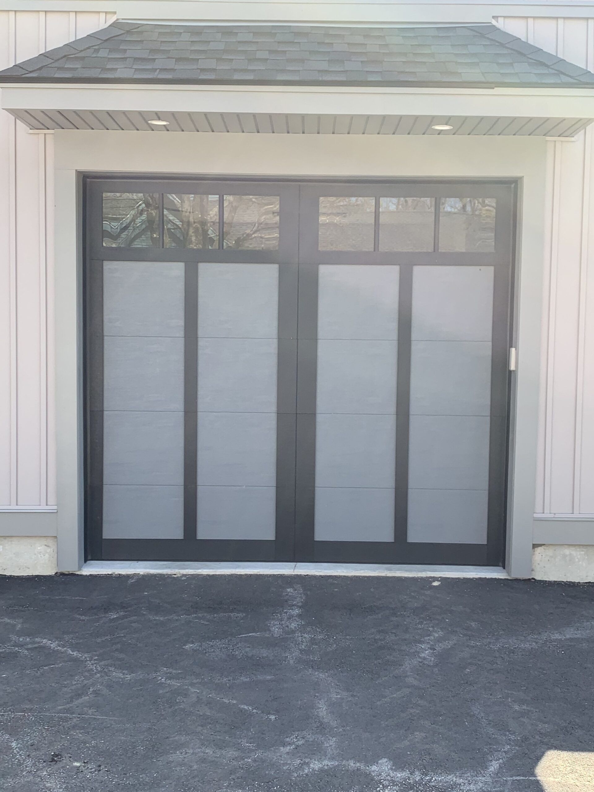 Black framed garage doors with frosted glass panels, set in a light gray exterior.