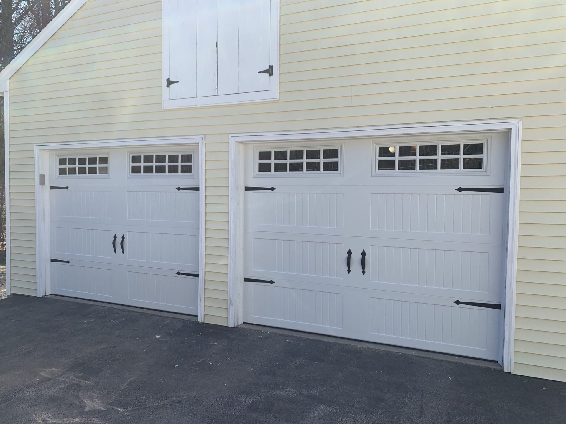 Two white garage doors with black hardware on a yellow building.