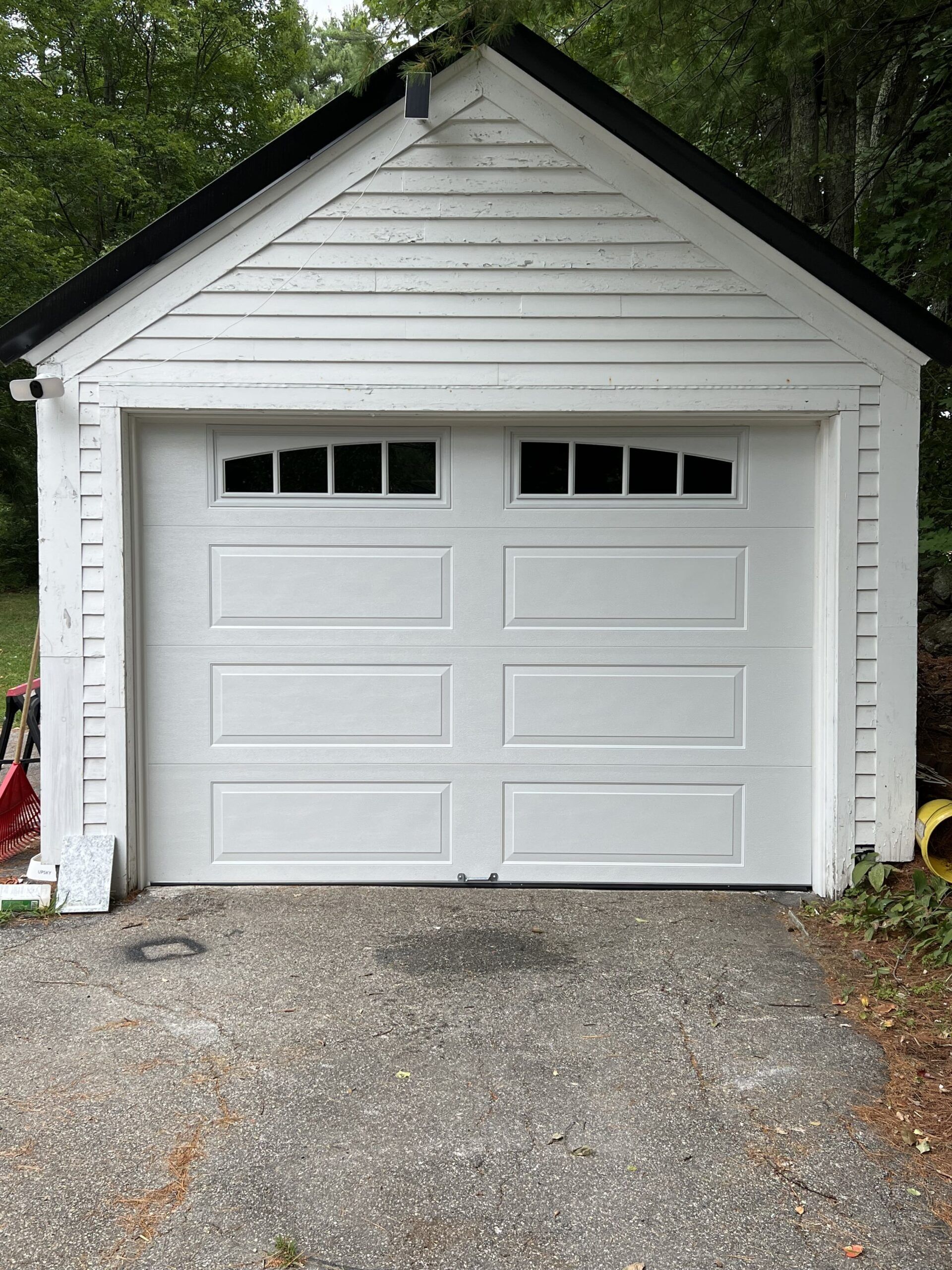 White garage with black trim and small windows. Gravel driveway.