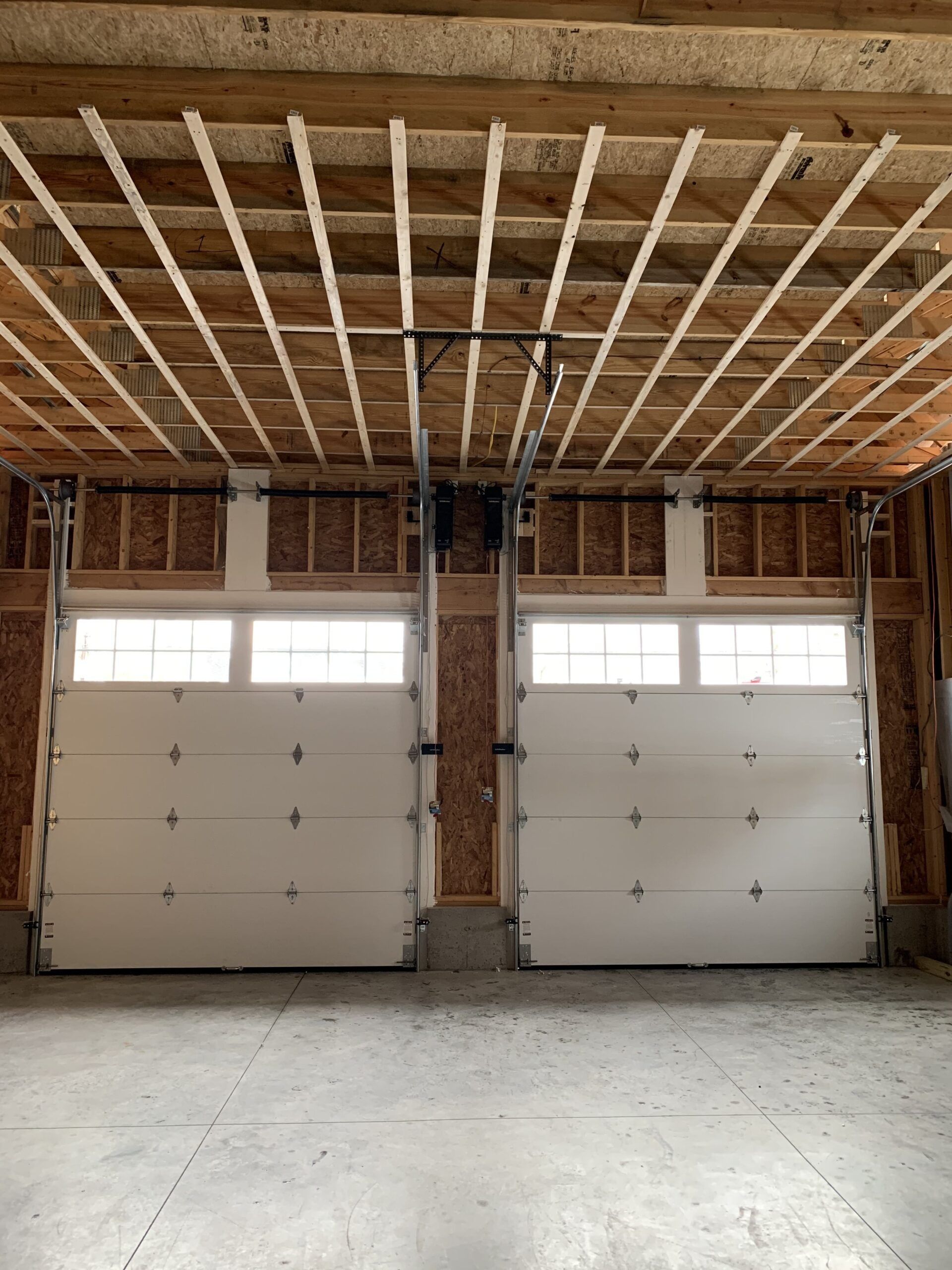 Two white garage doors in a garage with exposed wooden beams.