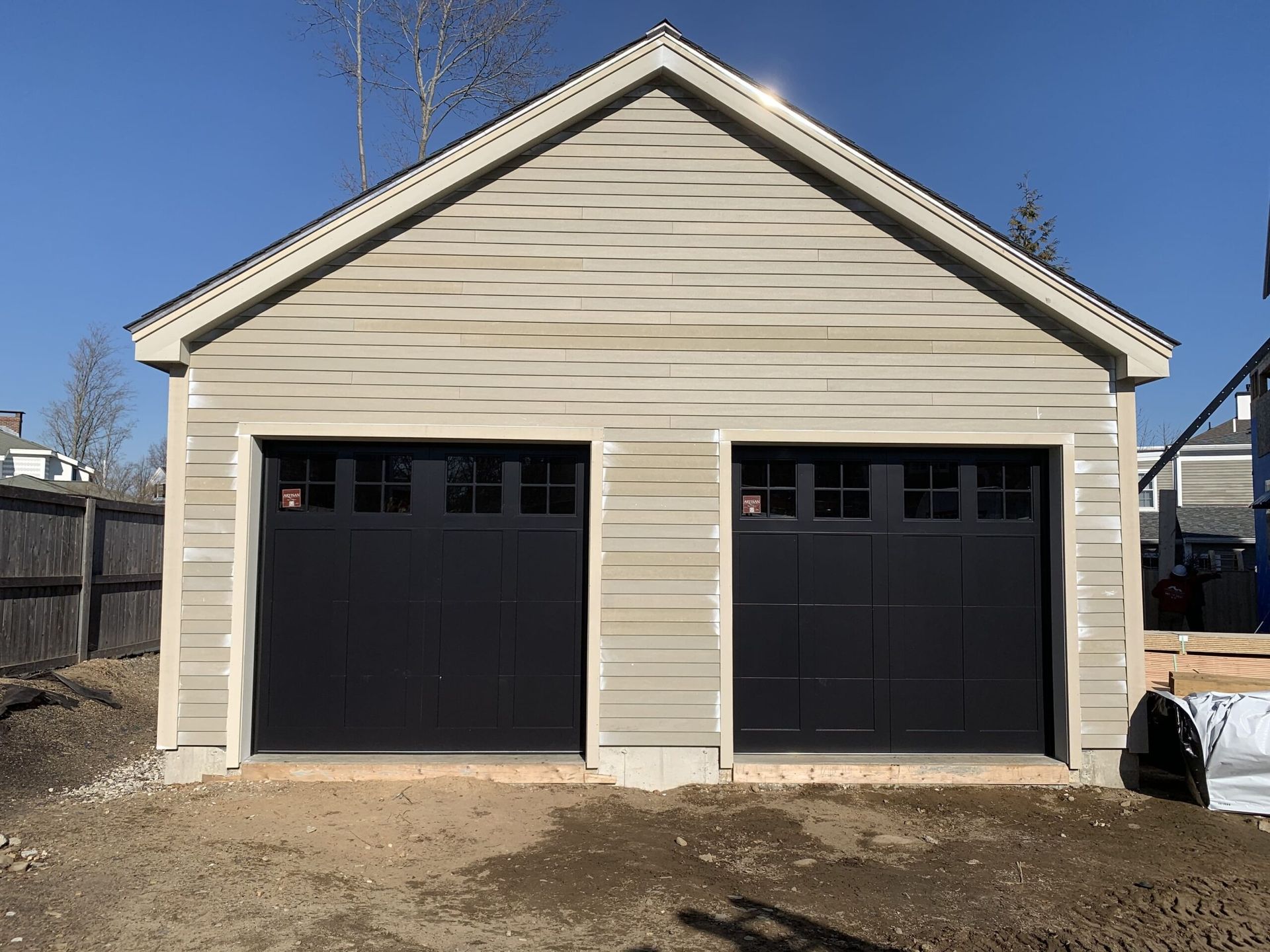 Two-car garage with black doors, beige siding, and a light blue sky in the background.