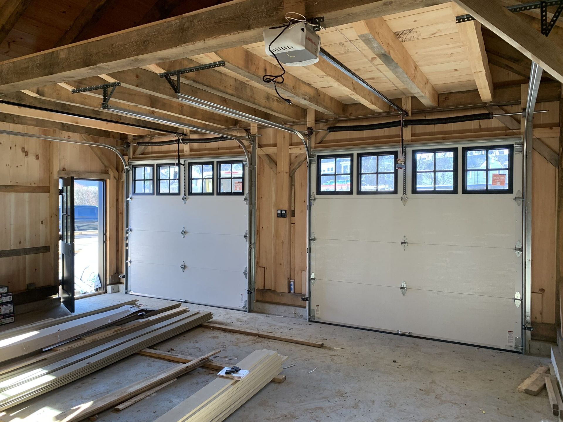 Interior view of unfinished garage with two white garage doors and window panels.
