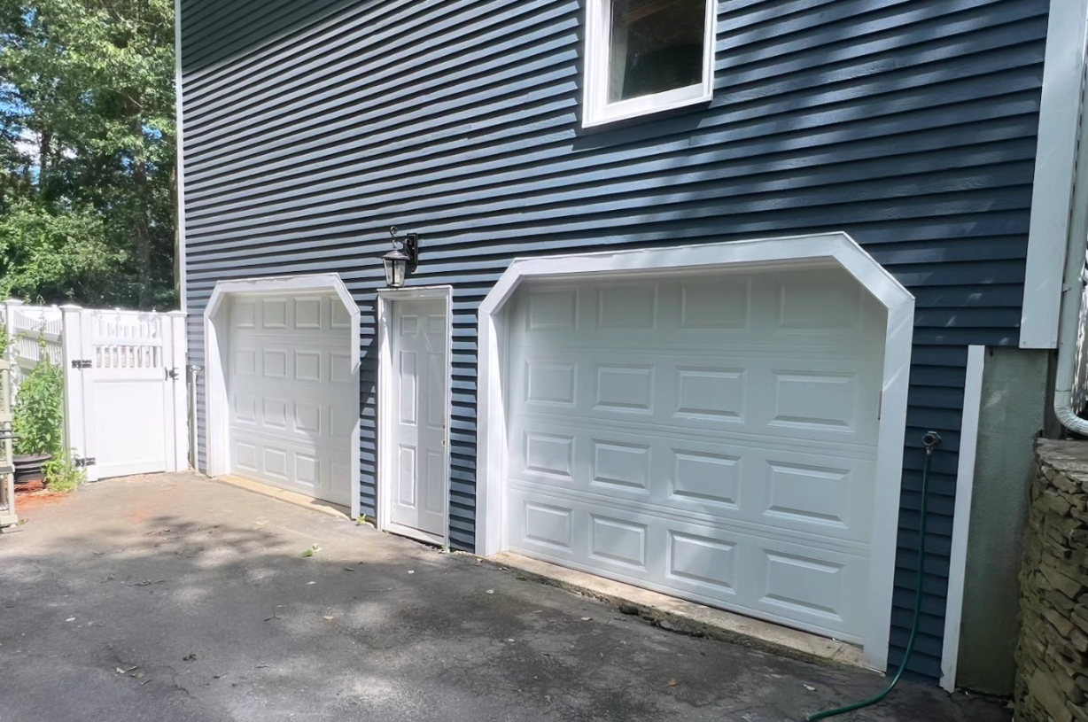 Blue house with two white garage doors, and a white door. Black asphalt driveway.