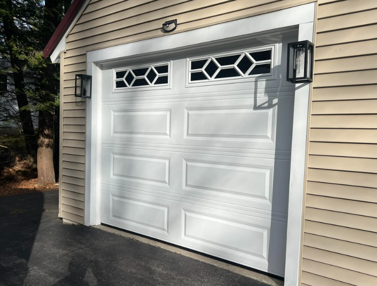White garage door with geometric glass panels and black sconces on a light-colored siding.