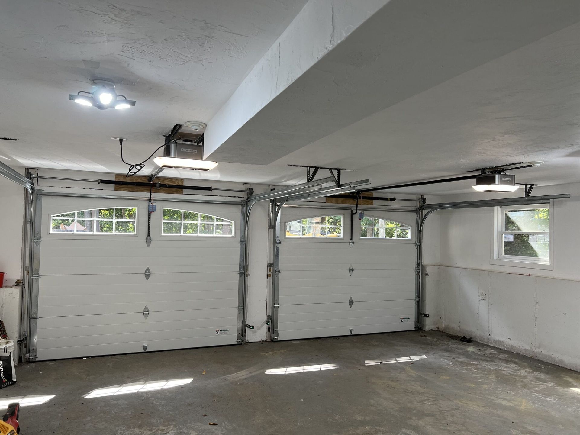 Two white garage doors inside a garage, with openers installed above.
