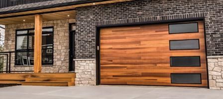 Modern home exterior with wood garage door, four windows, and brick facade.