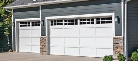 Two white garage doors with rectangular windows; blue-gray siding; stone accents.